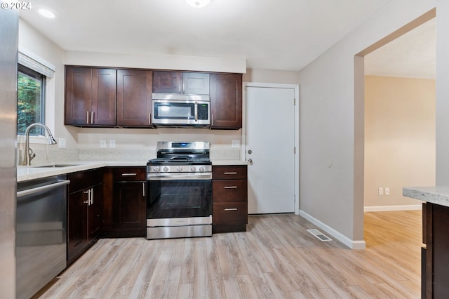 kitchen with sink, stainless steel appliances, light stone counters, light hardwood / wood-style floors, and dark brown cabinets