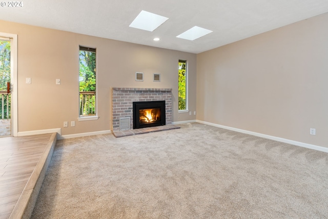 unfurnished living room featuring light hardwood / wood-style floors, a skylight, and a brick fireplace