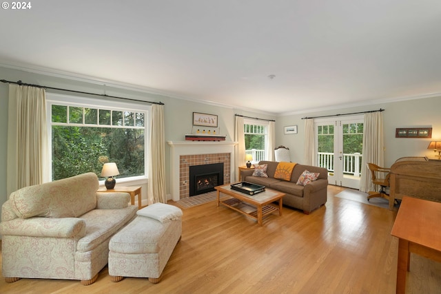 living room with light hardwood / wood-style flooring, a tiled fireplace, crown molding, and french doors