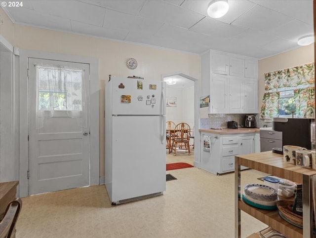 kitchen with white refrigerator, crown molding, decorative backsplash, and white cabinetry