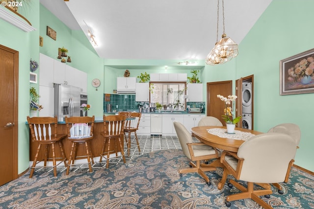 dining area featuring high vaulted ceiling, stacked washer and clothes dryer, a notable chandelier, and sink