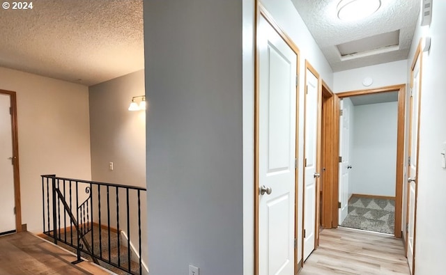 hallway with a textured ceiling and light hardwood / wood-style flooring