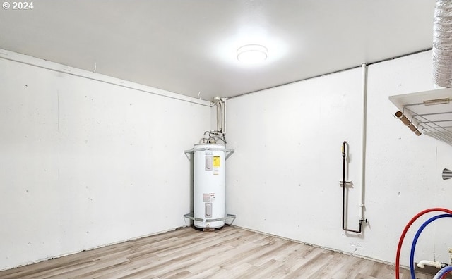 basement with light hardwood / wood-style floors and water heater