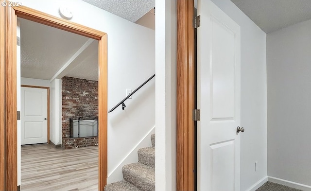 stairway featuring hardwood / wood-style flooring, a textured ceiling, and a brick fireplace