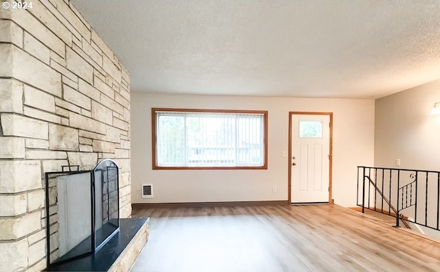 unfurnished living room with wood-type flooring, a textured ceiling, and a stone fireplace