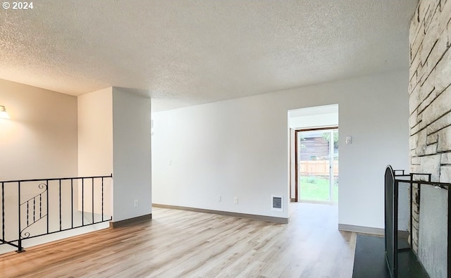 empty room featuring a large fireplace, a textured ceiling, and light hardwood / wood-style flooring