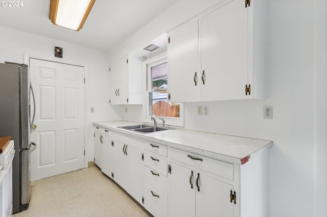 kitchen featuring stainless steel fridge, white cabinetry, and sink