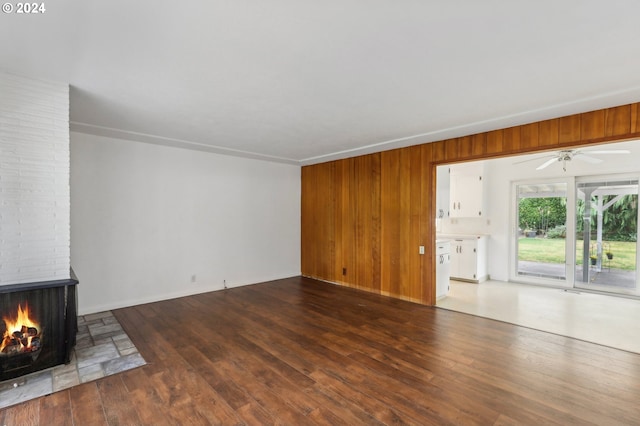 unfurnished living room featuring ceiling fan, dark hardwood / wood-style flooring, a fireplace, and wooden walls