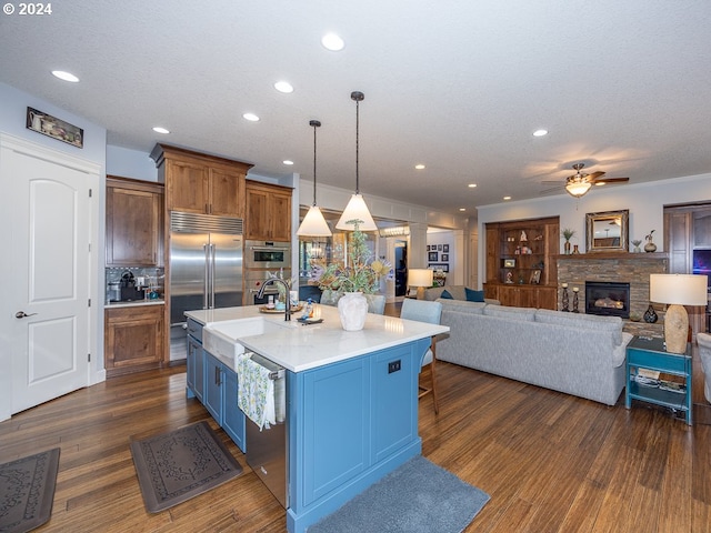 kitchen with ceiling fan, sink, hanging light fixtures, backsplash, and an island with sink