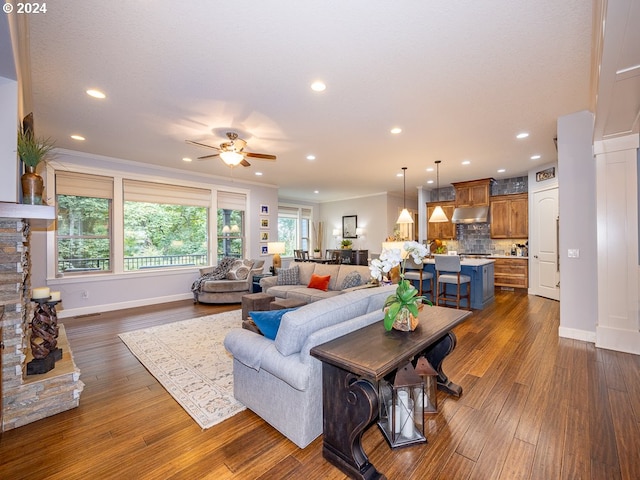 living room with dark hardwood / wood-style flooring, a stone fireplace, ceiling fan, and crown molding