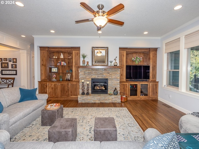 living room featuring ceiling fan, a textured ceiling, hardwood / wood-style flooring, a fireplace, and ornamental molding