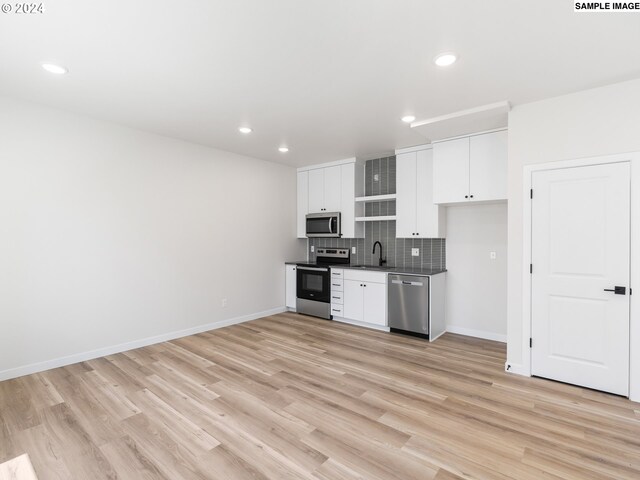 kitchen with white cabinets, sink, light wood-type flooring, appliances with stainless steel finishes, and tasteful backsplash