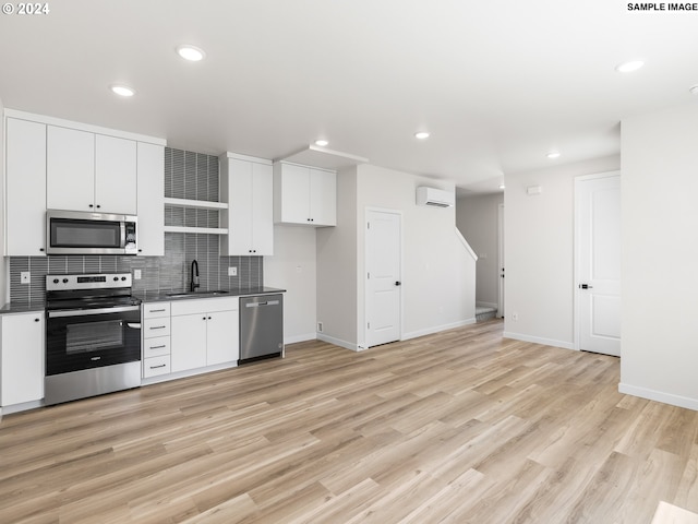 kitchen with stainless steel appliances, a wall unit AC, sink, white cabinets, and light hardwood / wood-style floors