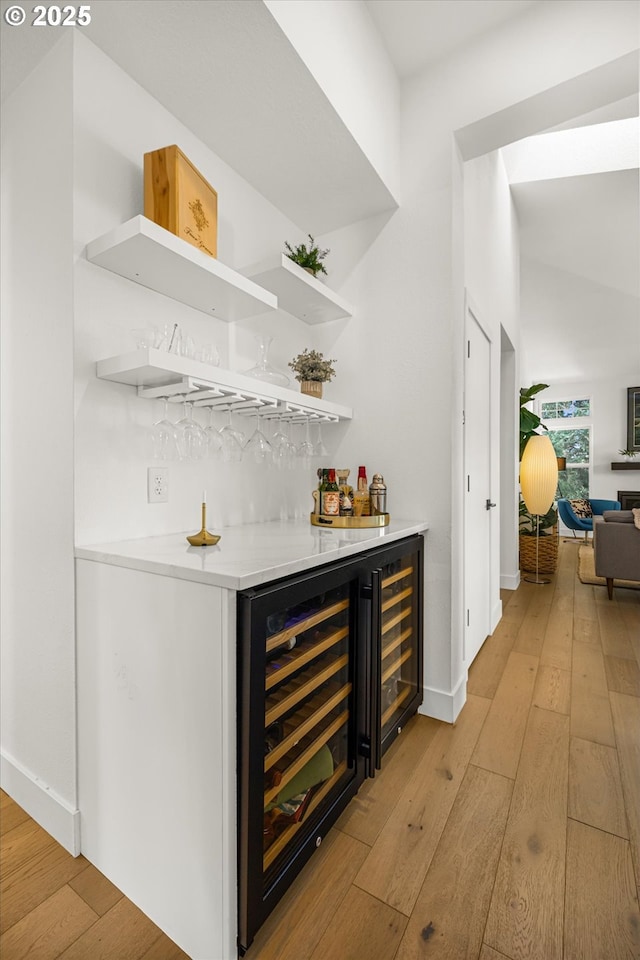 bar with a dry bar, light wood-style flooring, wine cooler, and baseboards