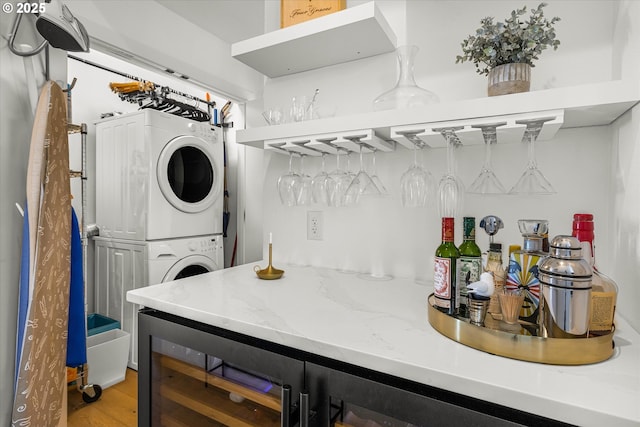 clothes washing area featuring light wood finished floors, laundry area, a bar, and stacked washer / drying machine