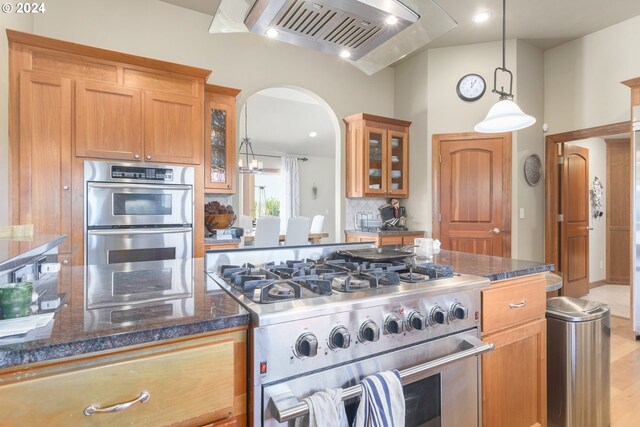 kitchen featuring hanging light fixtures, dark stone countertops, light wood-type flooring, and appliances with stainless steel finishes