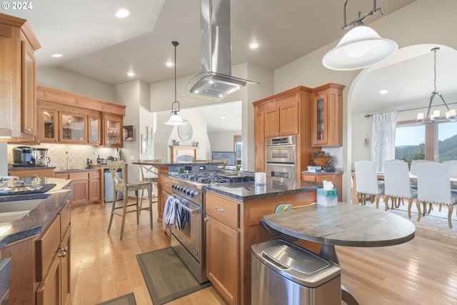 kitchen featuring stainless steel appliances, island range hood, a center island, hanging light fixtures, and light hardwood / wood-style floors