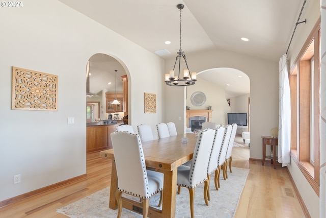 dining space with light wood-type flooring, a notable chandelier, and vaulted ceiling