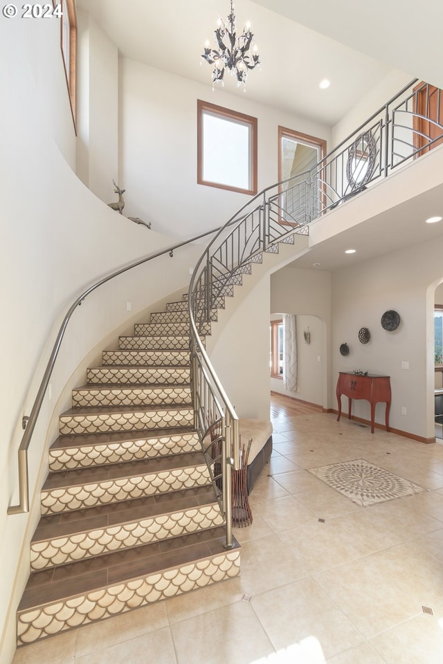 stairway featuring a wealth of natural light, a towering ceiling, tile patterned floors, and an inviting chandelier