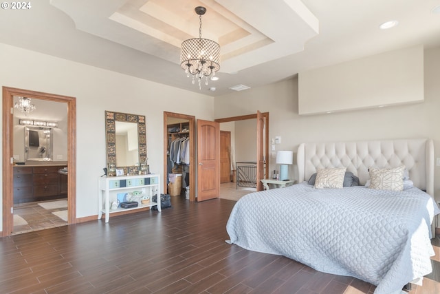 bedroom featuring a chandelier, ensuite bath, a tray ceiling, dark wood-type flooring, and a spacious closet