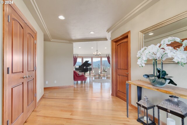 foyer with crown molding, a notable chandelier, and light wood-type flooring