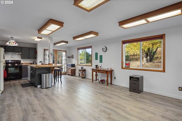 kitchen with a kitchen bar, white refrigerator, a center island, black range with electric stovetop, and light wood-type flooring