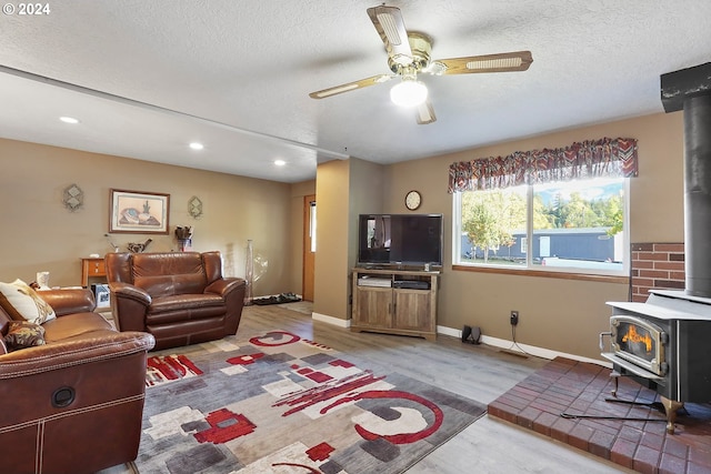 living room with ceiling fan, a wood stove, hardwood / wood-style floors, and a textured ceiling