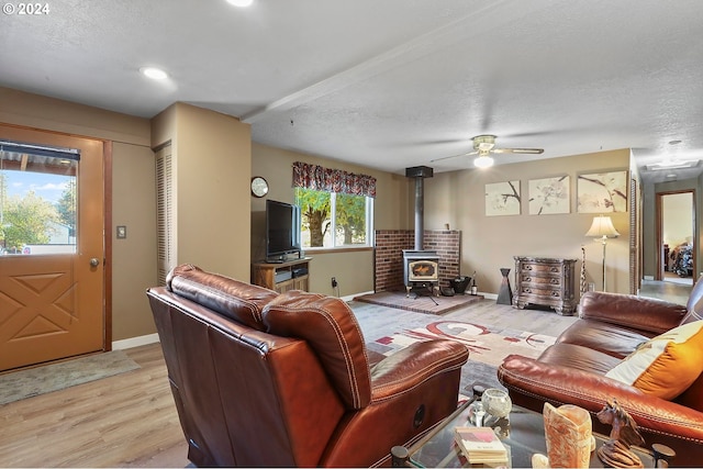 living room with ceiling fan, a wood stove, a textured ceiling, and light hardwood / wood-style flooring