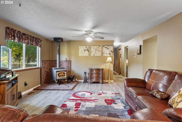 living room with a textured ceiling, light hardwood / wood-style floors, ceiling fan, and a wood stove