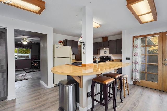 kitchen featuring a breakfast bar area, electric range, a wood stove, kitchen peninsula, and white fridge