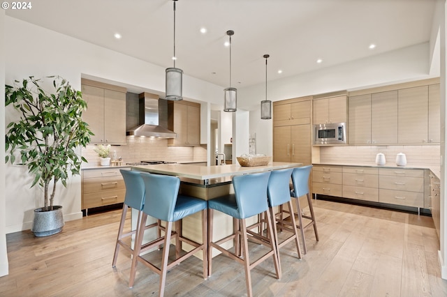kitchen with wall chimney exhaust hood, modern cabinets, a kitchen breakfast bar, tasteful backsplash, and light wood finished floors
