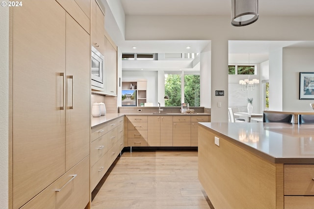 kitchen with light brown cabinetry, a sink, light wood-style floors, stainless steel microwave, and modern cabinets