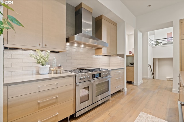 kitchen with range with two ovens, wall chimney exhaust hood, light countertops, backsplash, and light wood-style floors