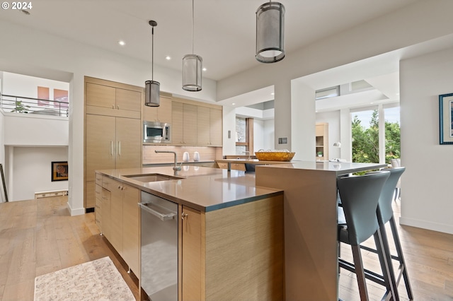 kitchen with a sink, appliances with stainless steel finishes, modern cabinets, a large island with sink, and light wood finished floors