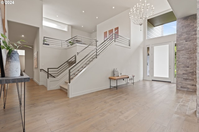 entryway with a towering ceiling, stairway, light wood-type flooring, a chandelier, and baseboards