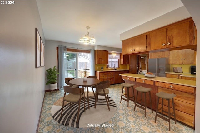 kitchen with a breakfast bar, an inviting chandelier, sink, hanging light fixtures, and stainless steel fridge with ice dispenser