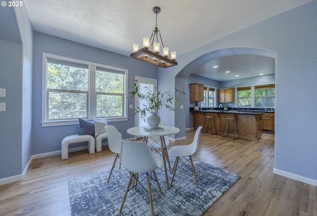 dining space with baseboards, arched walkways, and light wood-style floors