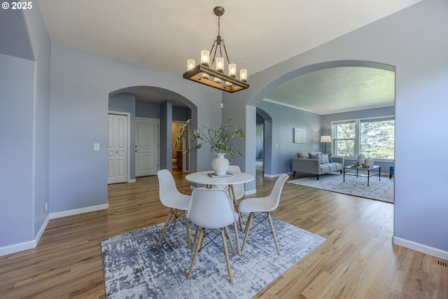 dining space with an inviting chandelier, arched walkways, baseboards, and light wood-type flooring