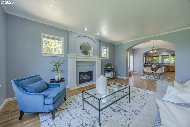 living area with crown molding, arched walkways, baseboards, and wood finished floors