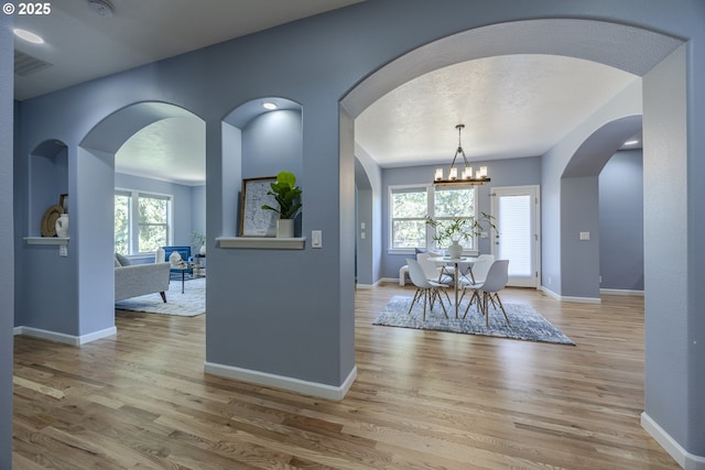 interior space with arched walkways, baseboards, an inviting chandelier, and wood finished floors