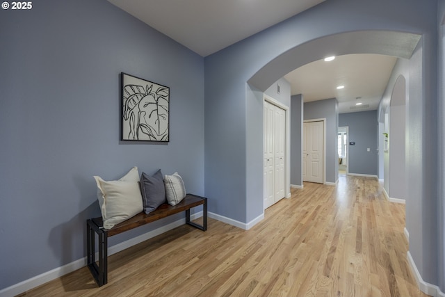 hallway featuring arched walkways, baseboards, recessed lighting, and light wood-style flooring