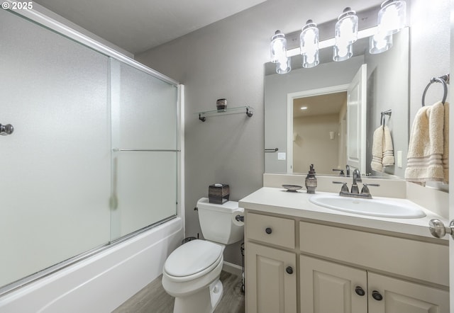 full bath with toilet, enclosed tub / shower combo, wood finished floors, and vanity