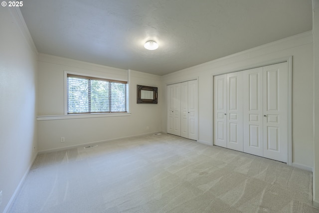 unfurnished bedroom featuring light colored carpet, baseboards, multiple closets, and ornamental molding