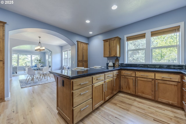kitchen with recessed lighting, a chandelier, brown cabinets, arched walkways, and light wood finished floors