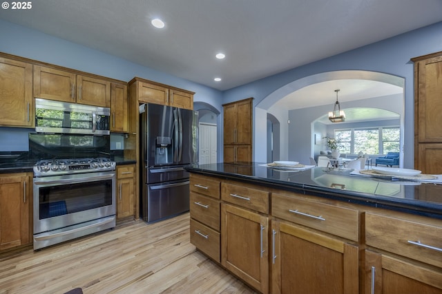 kitchen with brown cabinets, stainless steel appliances, arched walkways, and dark countertops