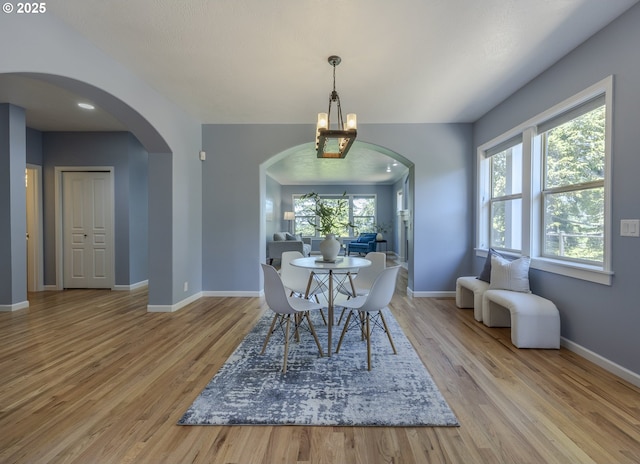 dining space featuring baseboards, arched walkways, wood finished floors, and a notable chandelier