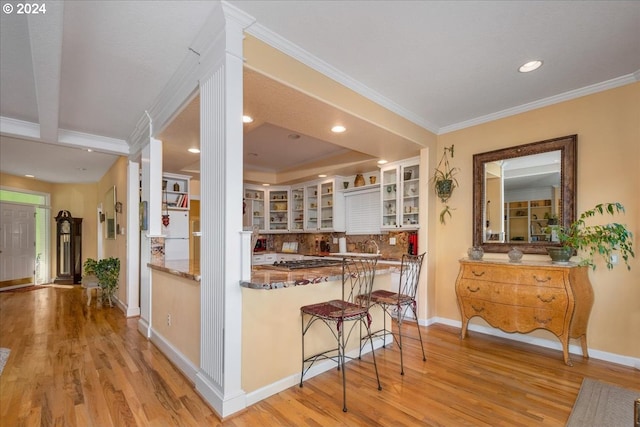 kitchen with light hardwood / wood-style flooring, kitchen peninsula, ornamental molding, tasteful backsplash, and a breakfast bar