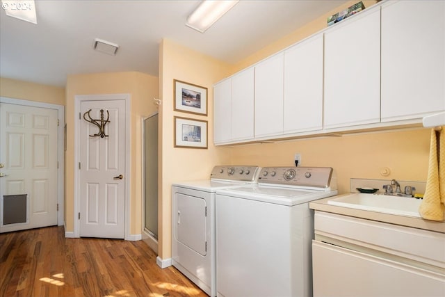 laundry area with washing machine and clothes dryer, cabinets, sink, and light wood-type flooring