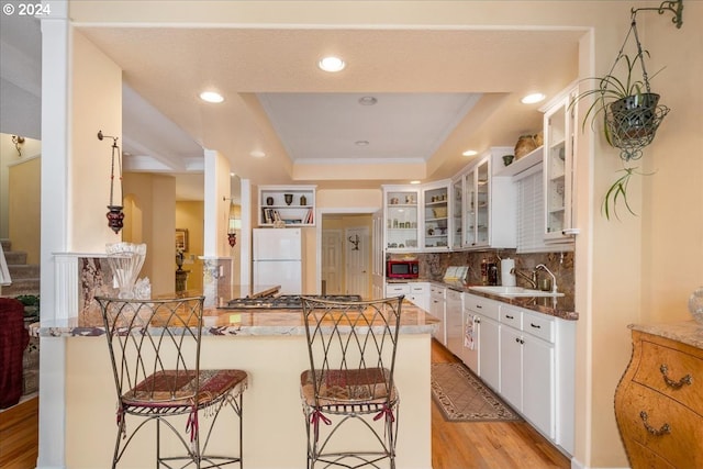 kitchen featuring a raised ceiling, kitchen peninsula, white cabinetry, white refrigerator, and light wood-type flooring