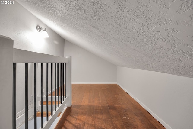 interior space with wood-type flooring, a textured ceiling, and vaulted ceiling